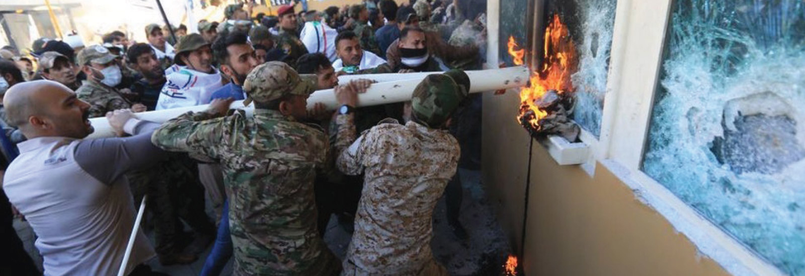 Image of large group of men attempting forced entry with objects and fire.